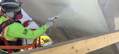 Man using spray gun to paint underside of a bridge pylon